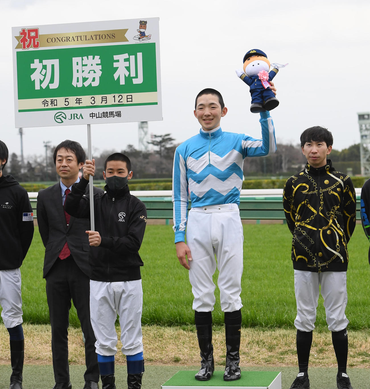 JRA初勝利を挙げ笑顔の小林勝騎手。左から2人目はプラカードを掲げる佐藤翔騎手（撮影・柴田隆二）