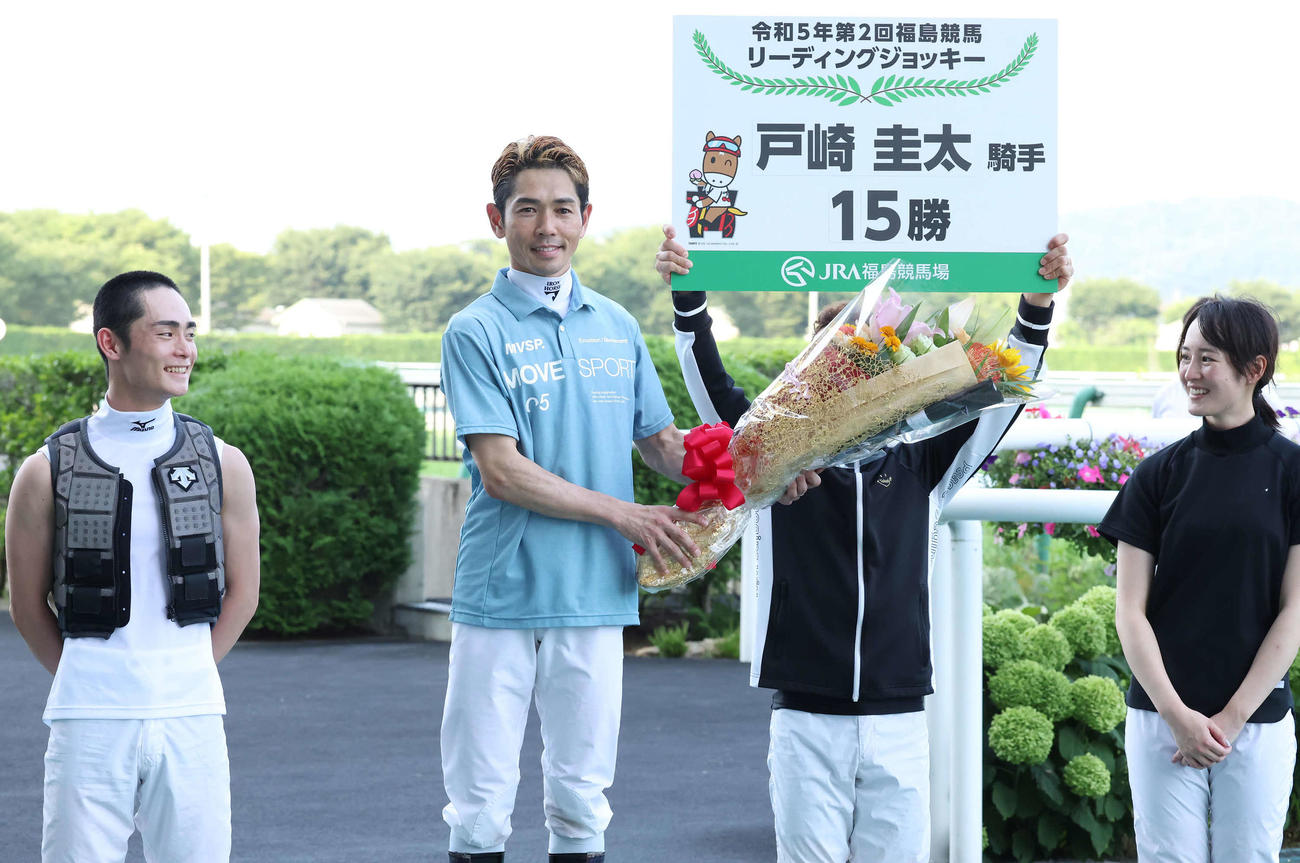 3年連続6回目の夏の福島リーディングを獲得した戸崎騎手（左から2人目）はボードを掲げる藤懸騎手の顔を花束で隠す（撮影・丹羽敏通）