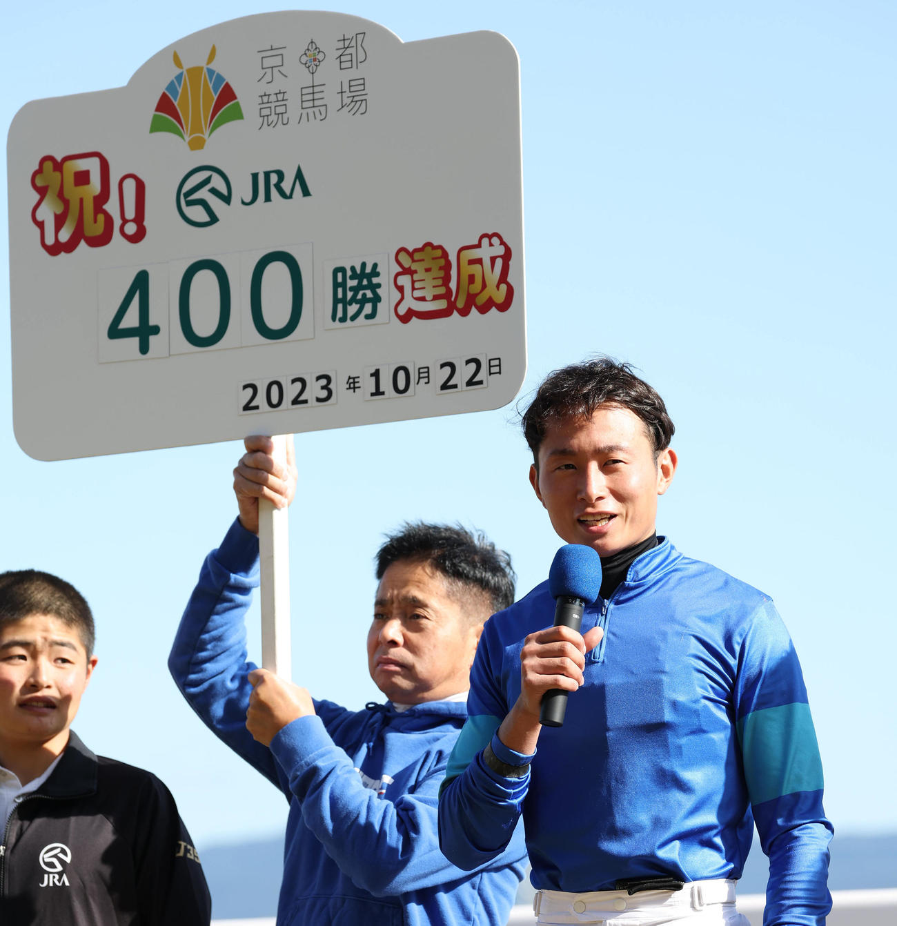 京都8R、JRA通算400勝を達成し笑顔でインタビューに答える岩田望騎手。中央は記念ボードを持つ父の岩田康騎手（撮影・白石智彦）