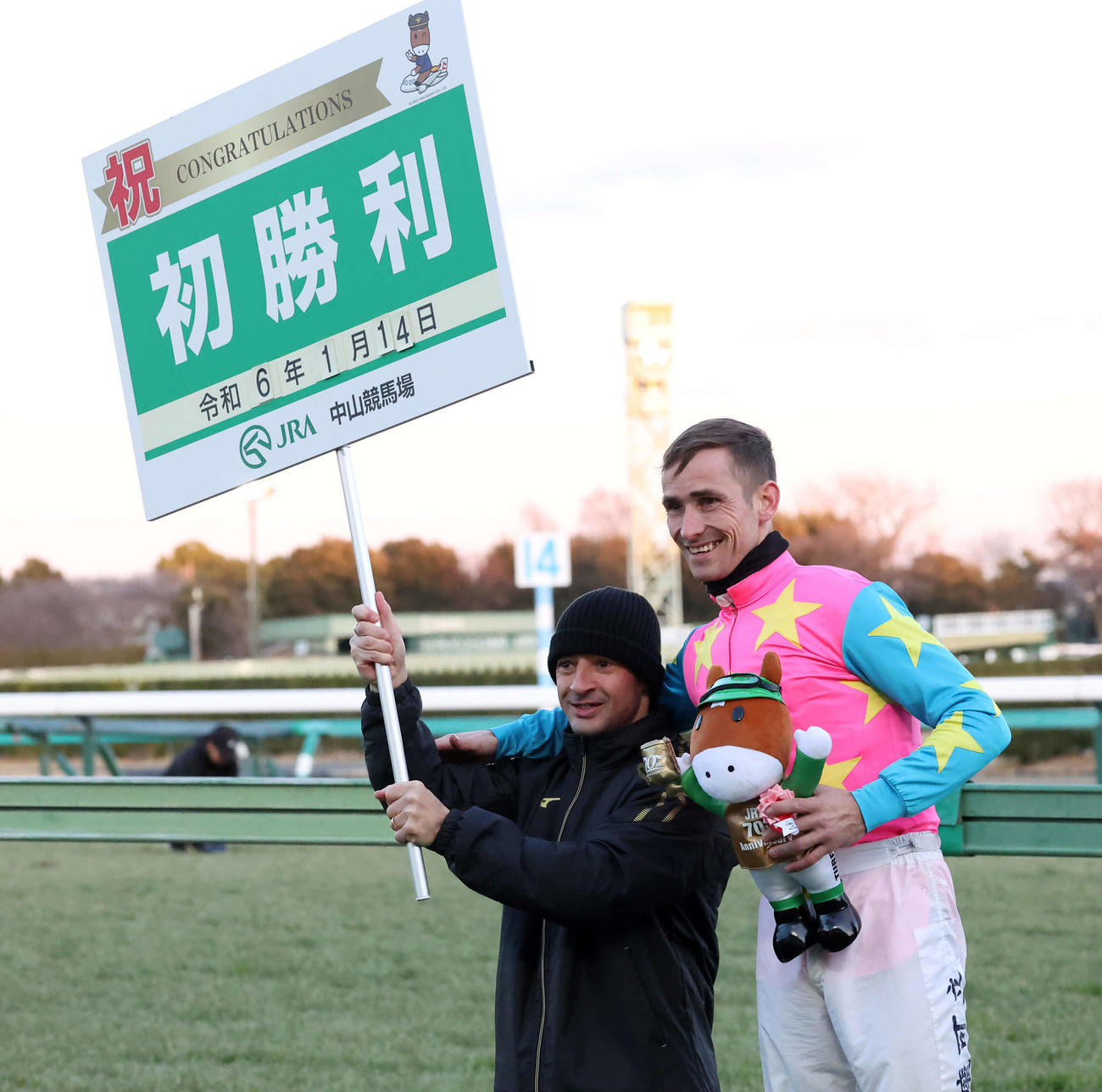 中山12Rで勝利して、初勝利のボードを掲げるルメール騎手（左）と写真に納まるピーヒュレク騎手
