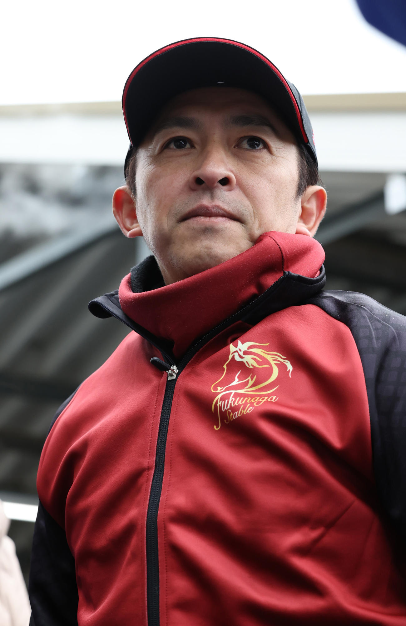調教を終え、囲み取材を受ける福永師　厩舎服の胸にはガンダムのシャア専用をモチーフにしたエンブレム