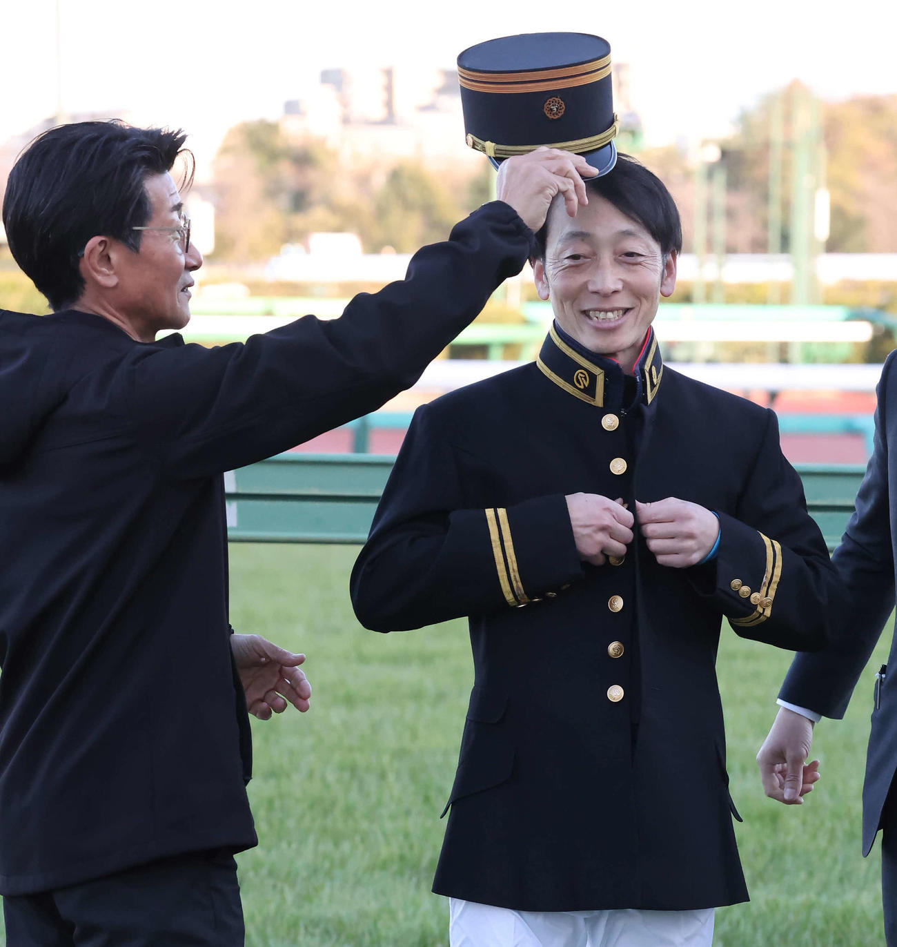 教官の制服を着て柴田善騎手（左）から帽子をかぶせてもらう武士沢騎手（撮影・丹羽敏通）