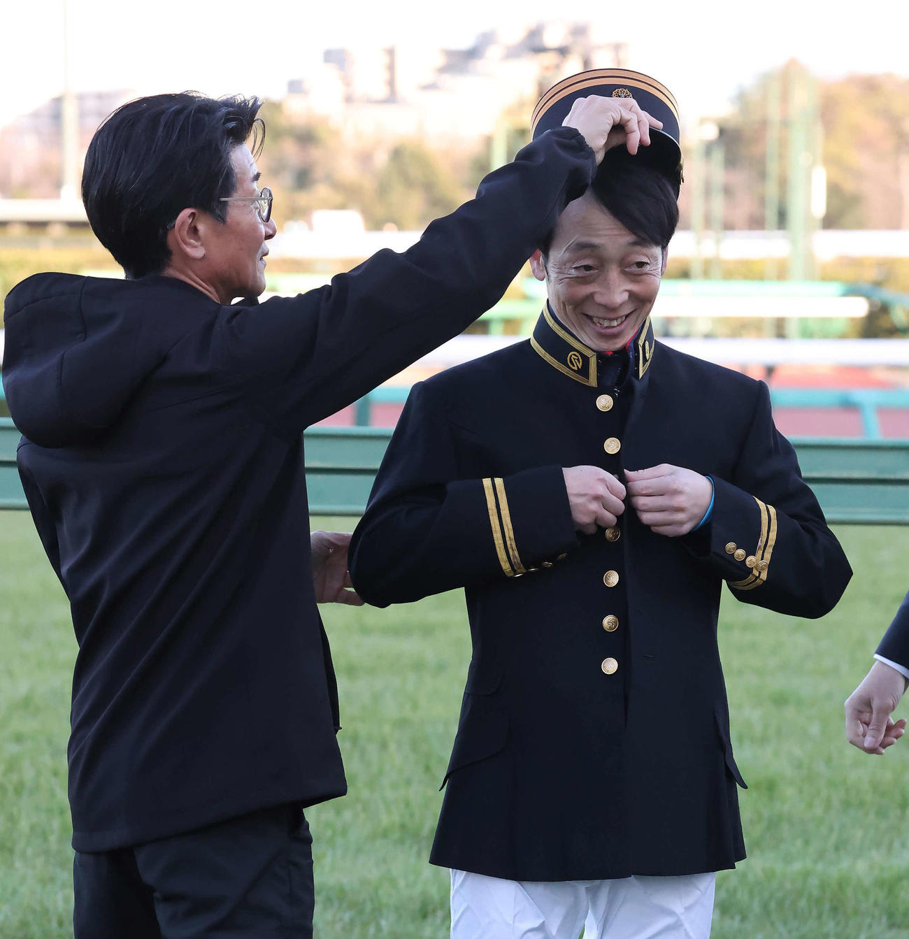 教官の制服を着て柴田善騎手（左）から帽子をかぶせてもらう武士沢騎手（撮影・丹羽敏通）
