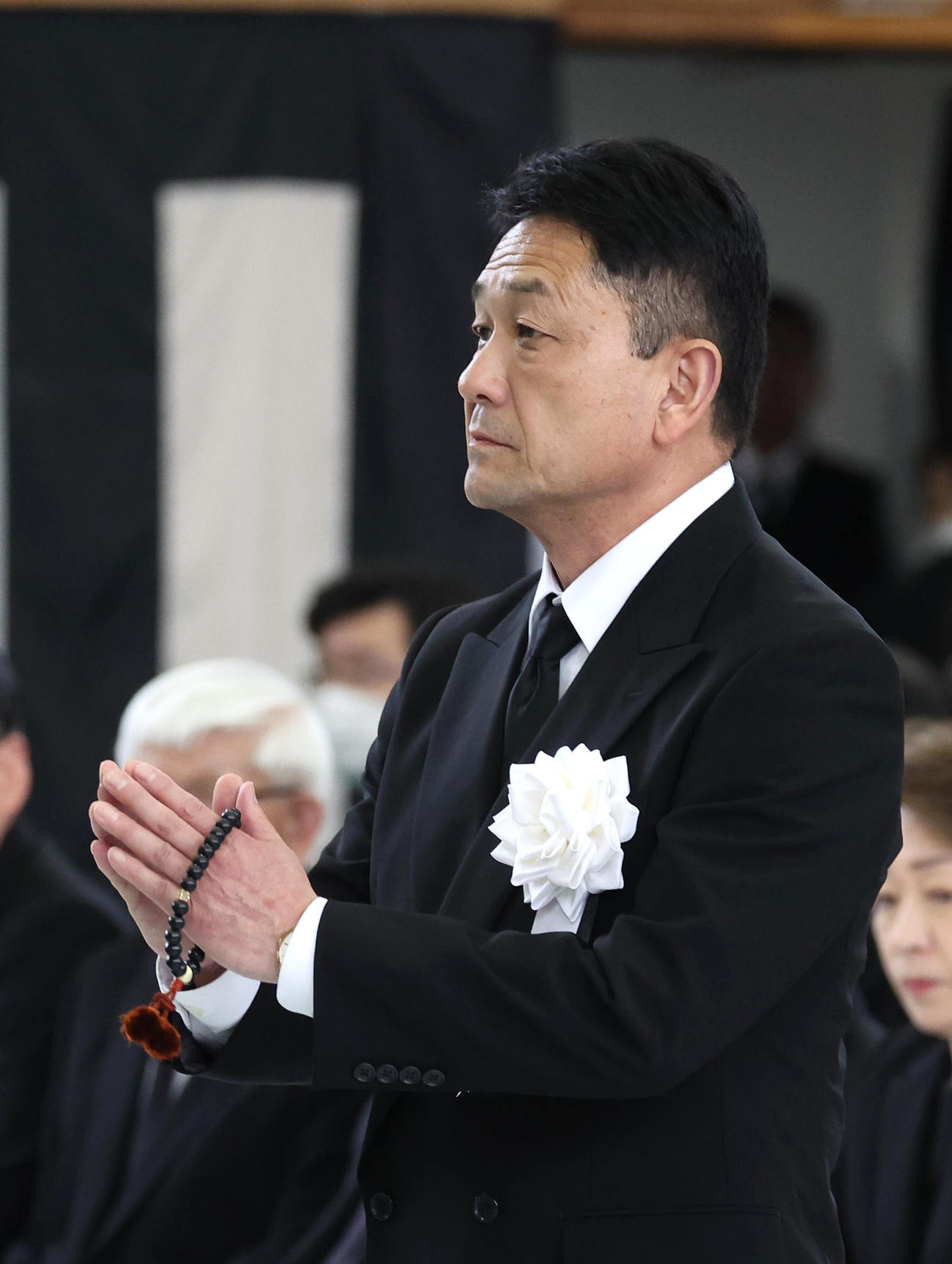 故藤岡康騎手の合同葬で焼香台の前で手を合わせ祭壇を見つめる父の藤岡師（撮影・白石智彦）