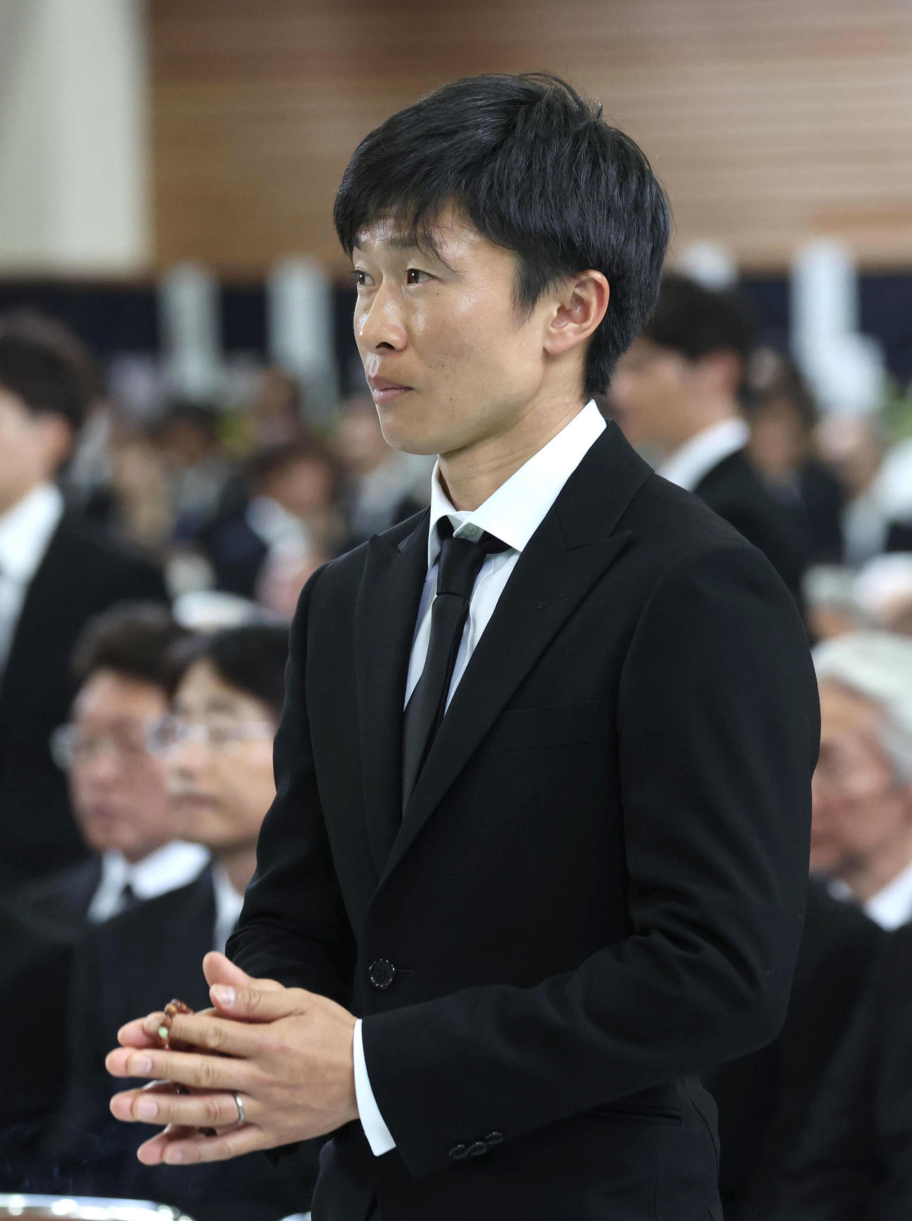故藤岡康騎手の合同葬で焼香台の前で手を合わせ祭壇を見つめる荻野琢騎手（撮影・白石智彦）