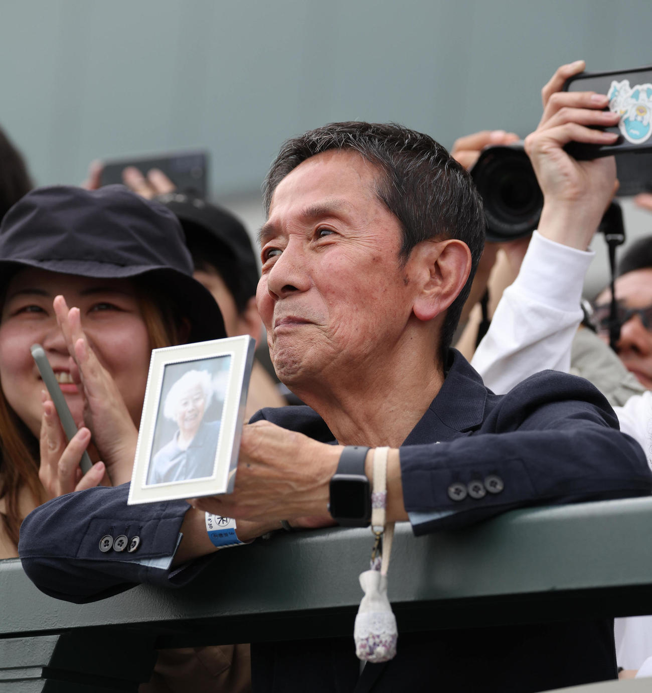 祖母の田鶴子さんの遺影を手にヒーローインタビューを聞く菱田騎手の父の寿男さん（撮影・白石智彦）