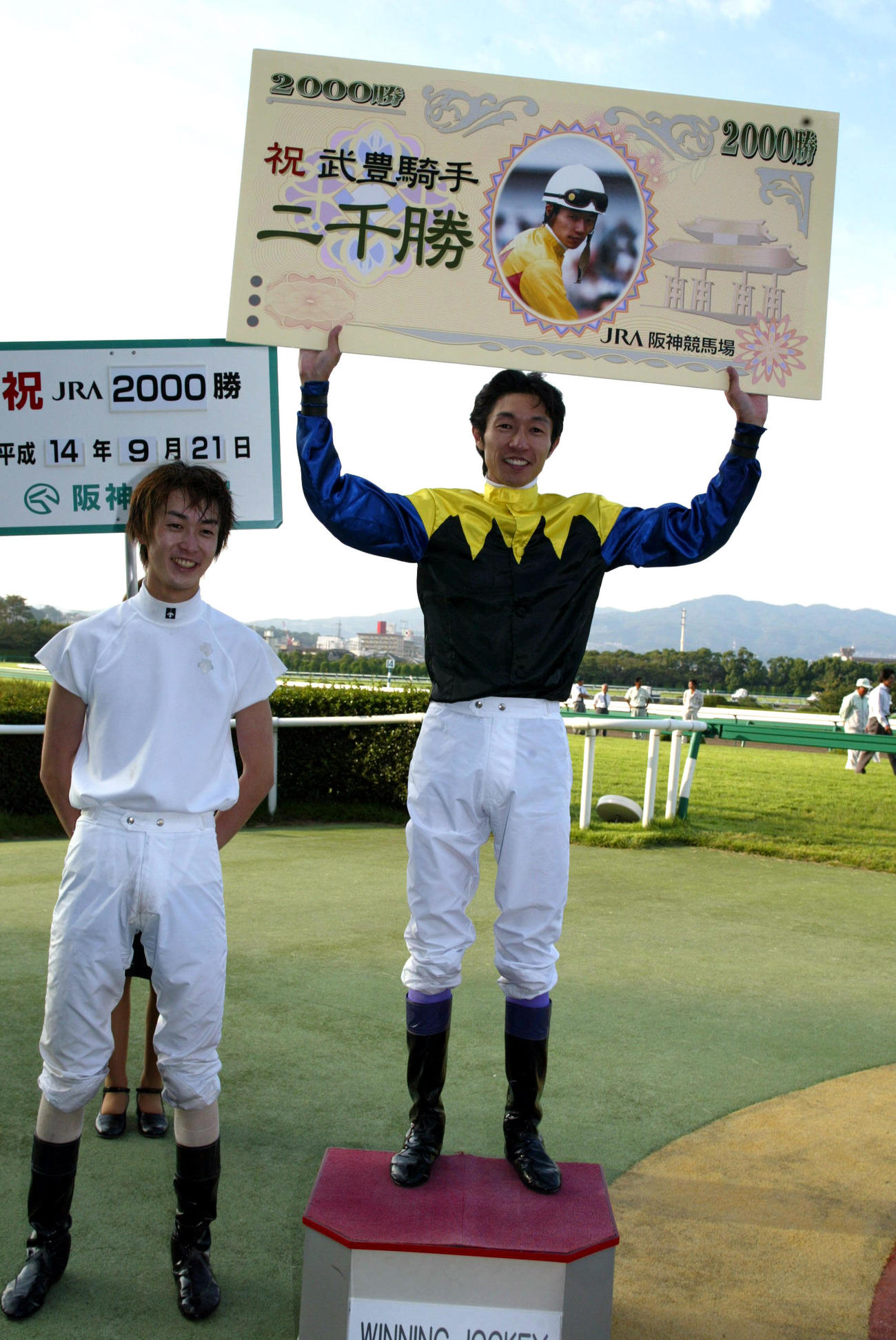 02年9月、弟幸四郎騎手の祝福を受け、通算2000勝のボードを掲げる武豊騎手