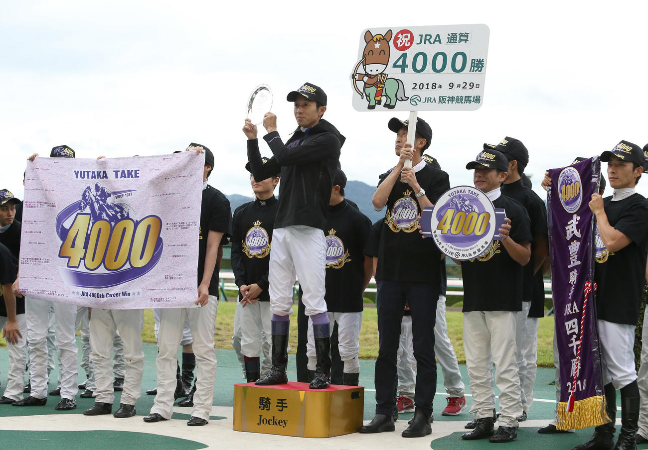 18年9月、記念プレートを掲げ笑顔の武豊騎手（中央）。右からレイを持つ川田騎手、ボードを持つ四位騎手