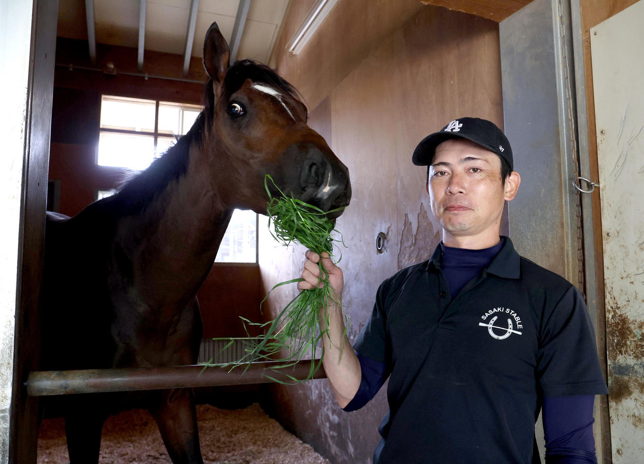 青草を食べる東京ダービーを制したラムジェットと担当の高木助手（撮影・白石智彦）