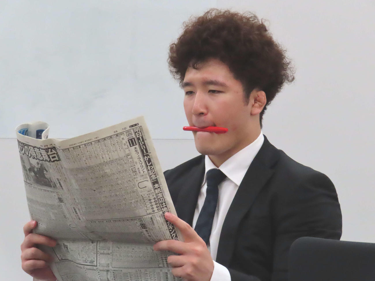赤ペンをくわえ、真剣に予想する深田雄智記者