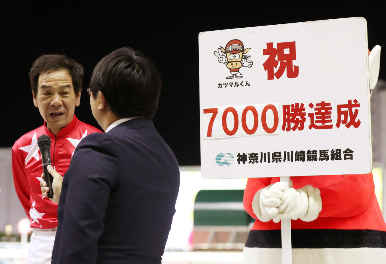 地方通算7000勝を達成した的場文男騎手（左）は祝福ボードを横にインタビューを受ける（撮影・松本俊）