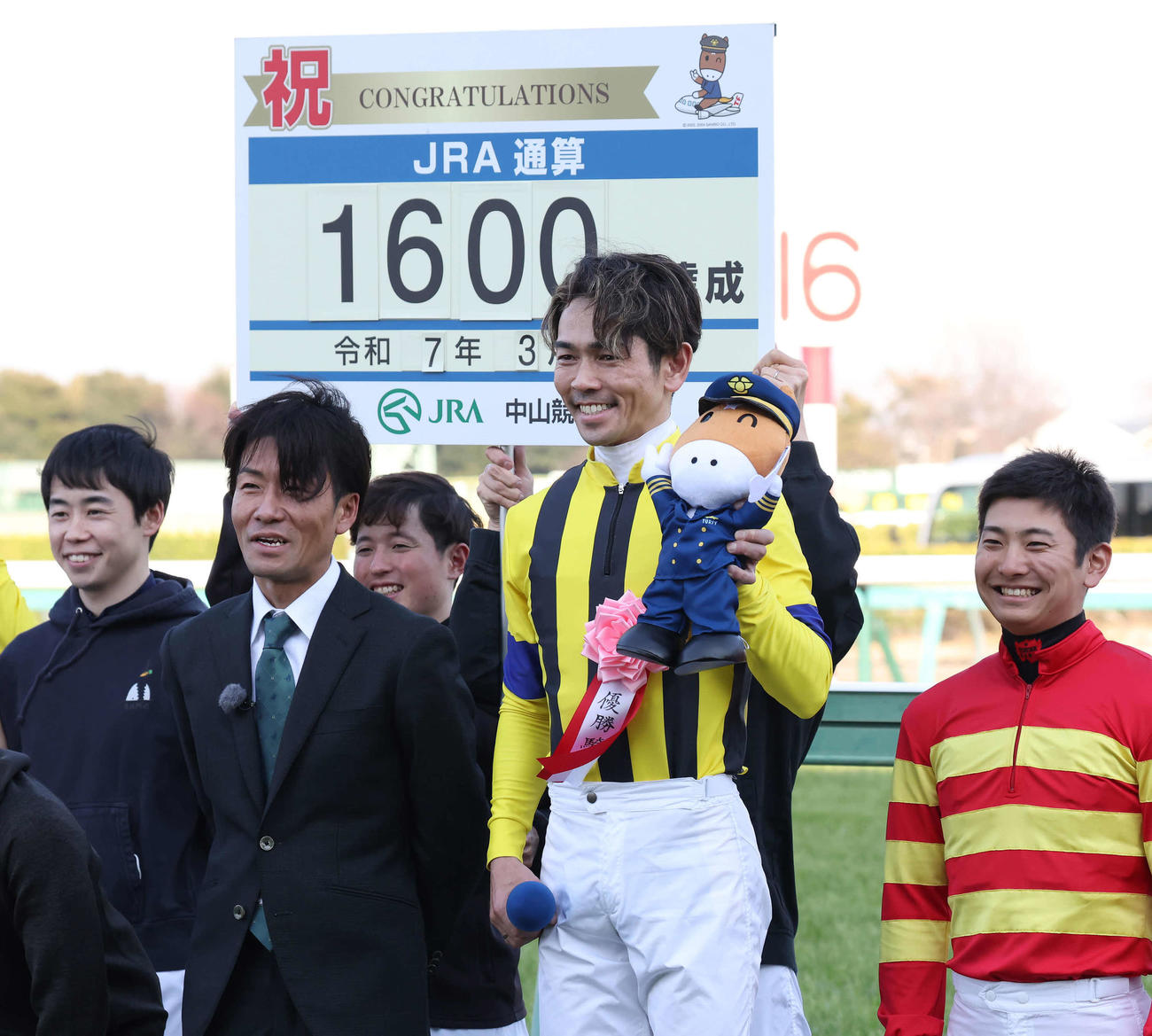 JRA通算1600勝を達成して笑顔を見せる戸崎騎手。左は元騎手の森泰斗氏（撮影・丹羽敏通）
