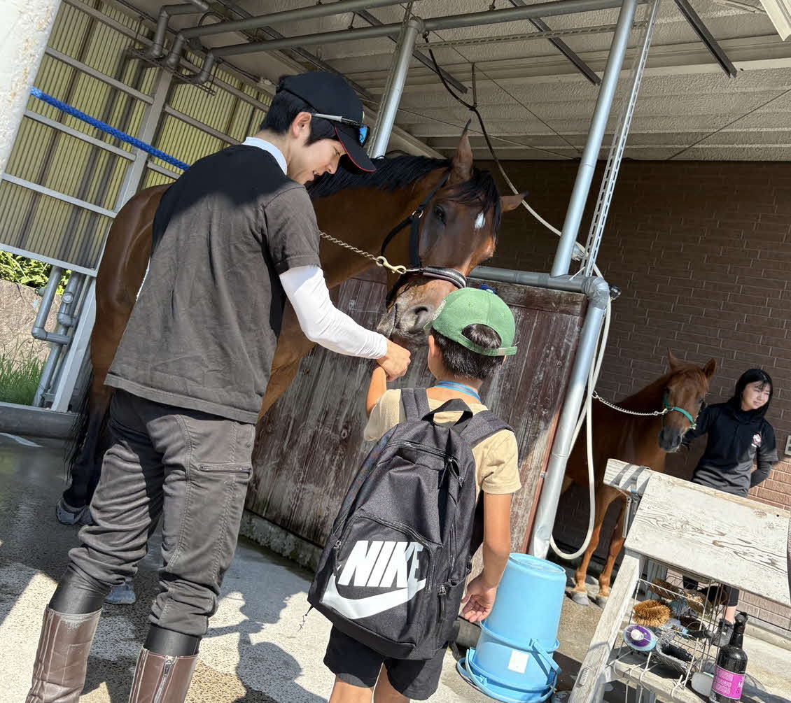 ツアー参加した子どもと一緒に馬にニンジンをあげる小崎騎手