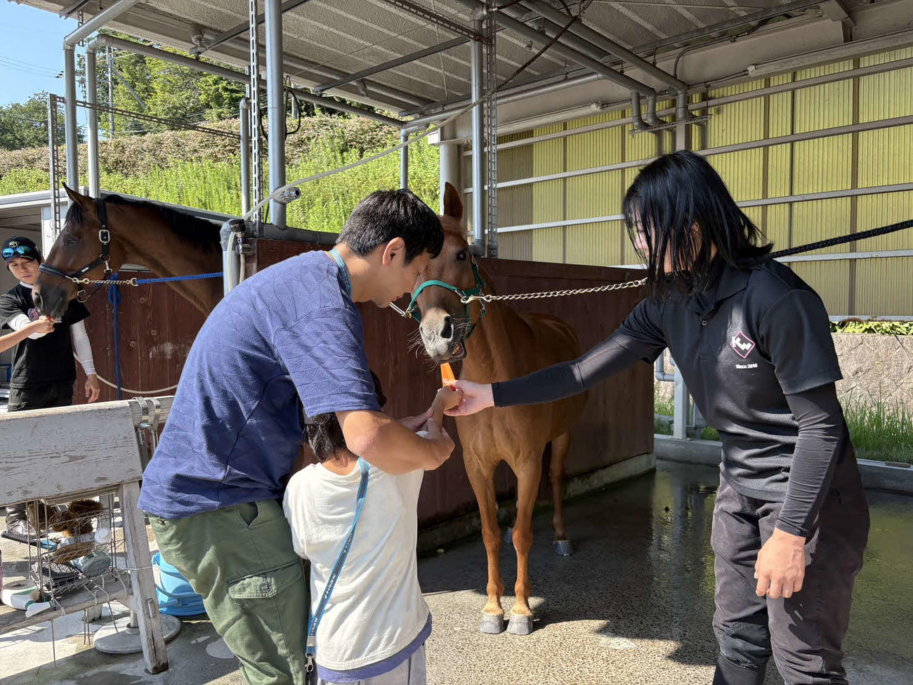ツアーに参加した親子と一緒に馬にニンジンをあげる河原田菜々騎手