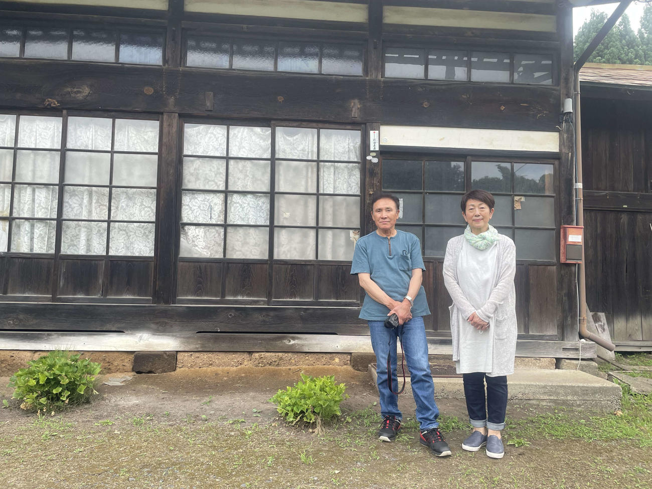前田長吉の生家の前に立つ、甥孫の前田貞直さん（左）と妻ツヱ子さん