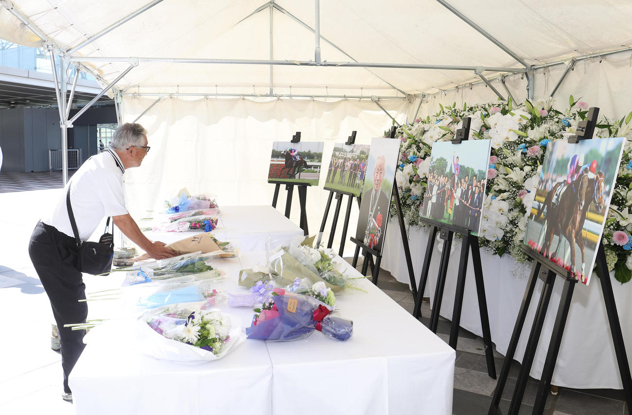 阪神競馬場に設置された松本好雄オーナーの献花台に花を手向けるファン（撮影・白石智彦）