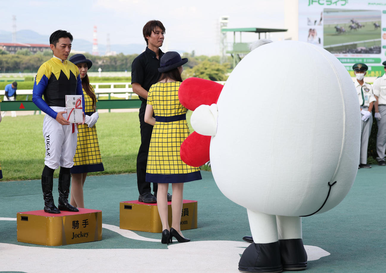 表彰台からカンテレのマスコットキャラ・ハチエモンを見つめる川田騎手（撮影・白石智彦）