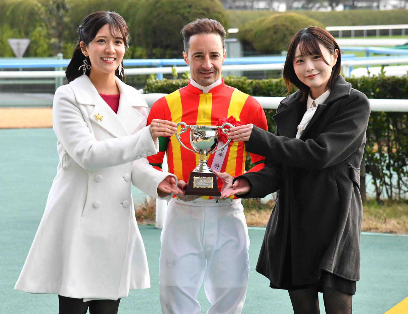 2025アンバサダーの石川彩夏（左）、小倉競馬2026アンバサダーのHKT48市村愛里（右）と記念撮影するルメール騎手（撮影・岩下翔太）