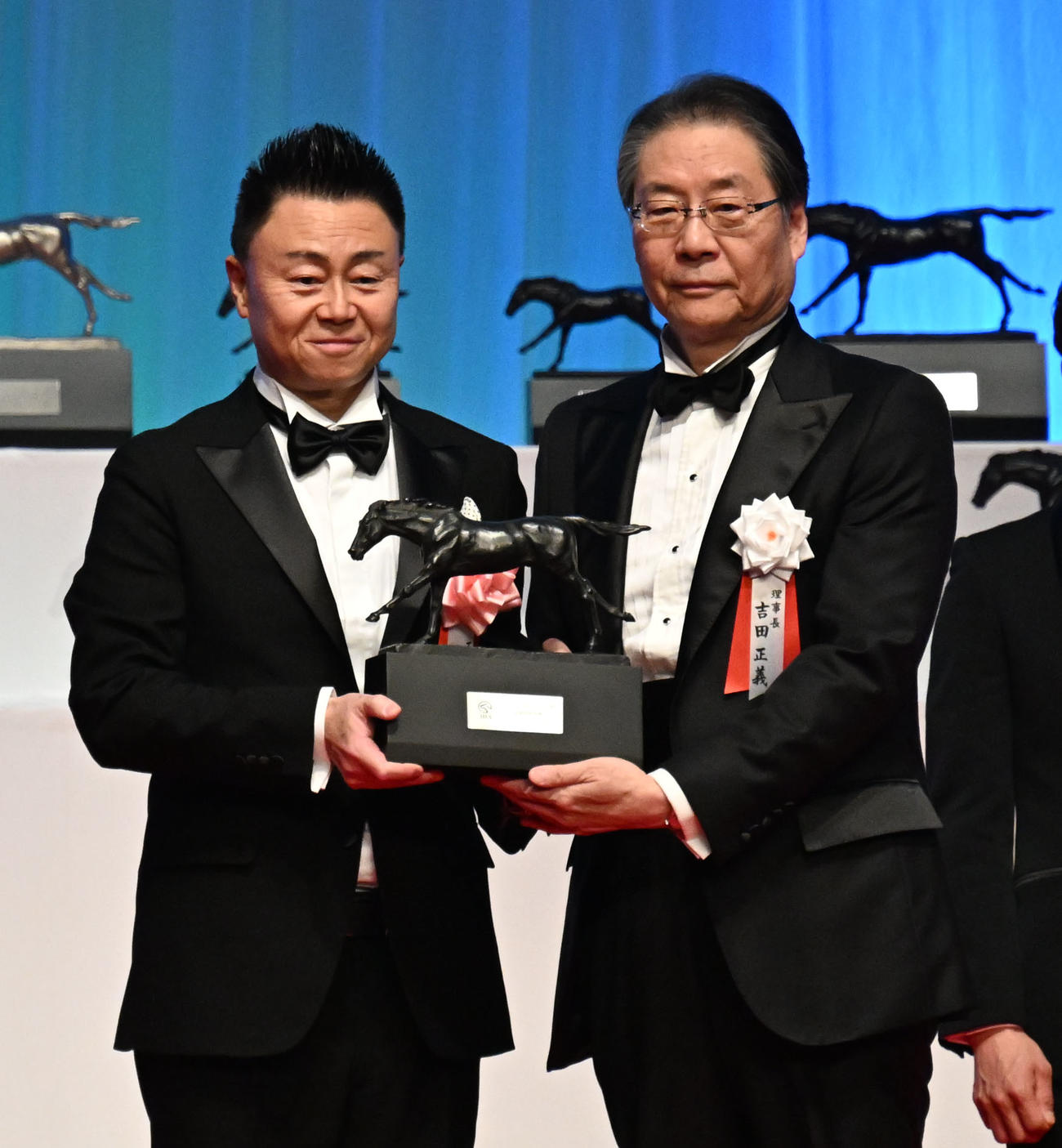 2025年度JRA賞授賞式　エコロデュエルで最優秀障害馬賞を受賞し、JRAの吉田理事長からトロフィーを受け取る馬主の原村氏（左）（撮影・千葉一成）