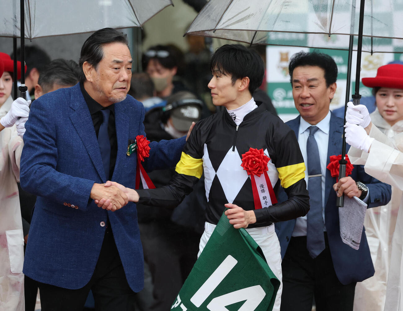 廣崎利洋オーナー（左）と握手をしながらウイナーズサークルヘ向かう坂井騎手。右は藤原師（撮影・白石智彦）