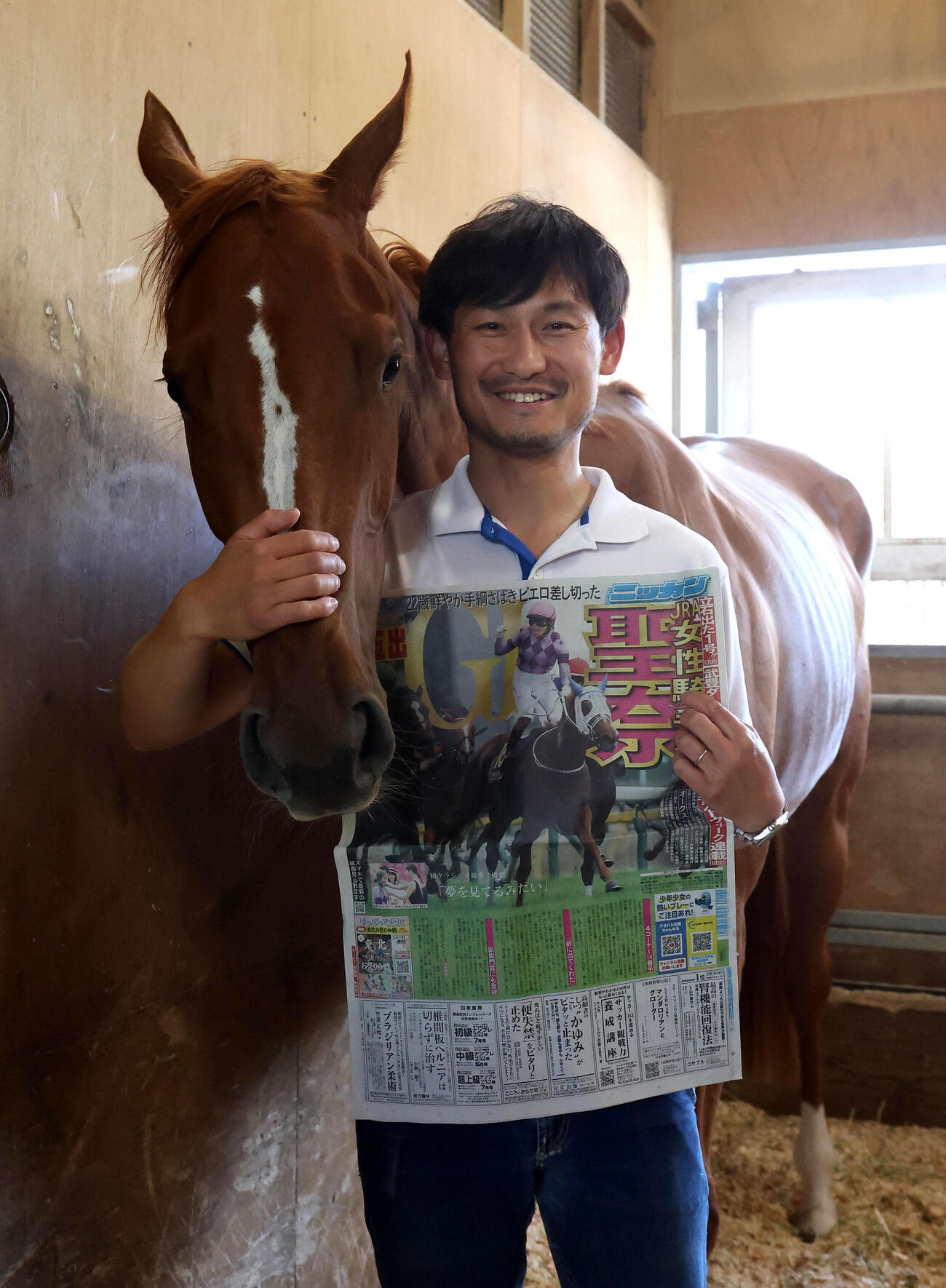 オークス制覇を報じる日刊スポーツの一面を掲げる担当の佐々木邦幸調教助手とジュウリョクピエロ（撮影・白石智彦）