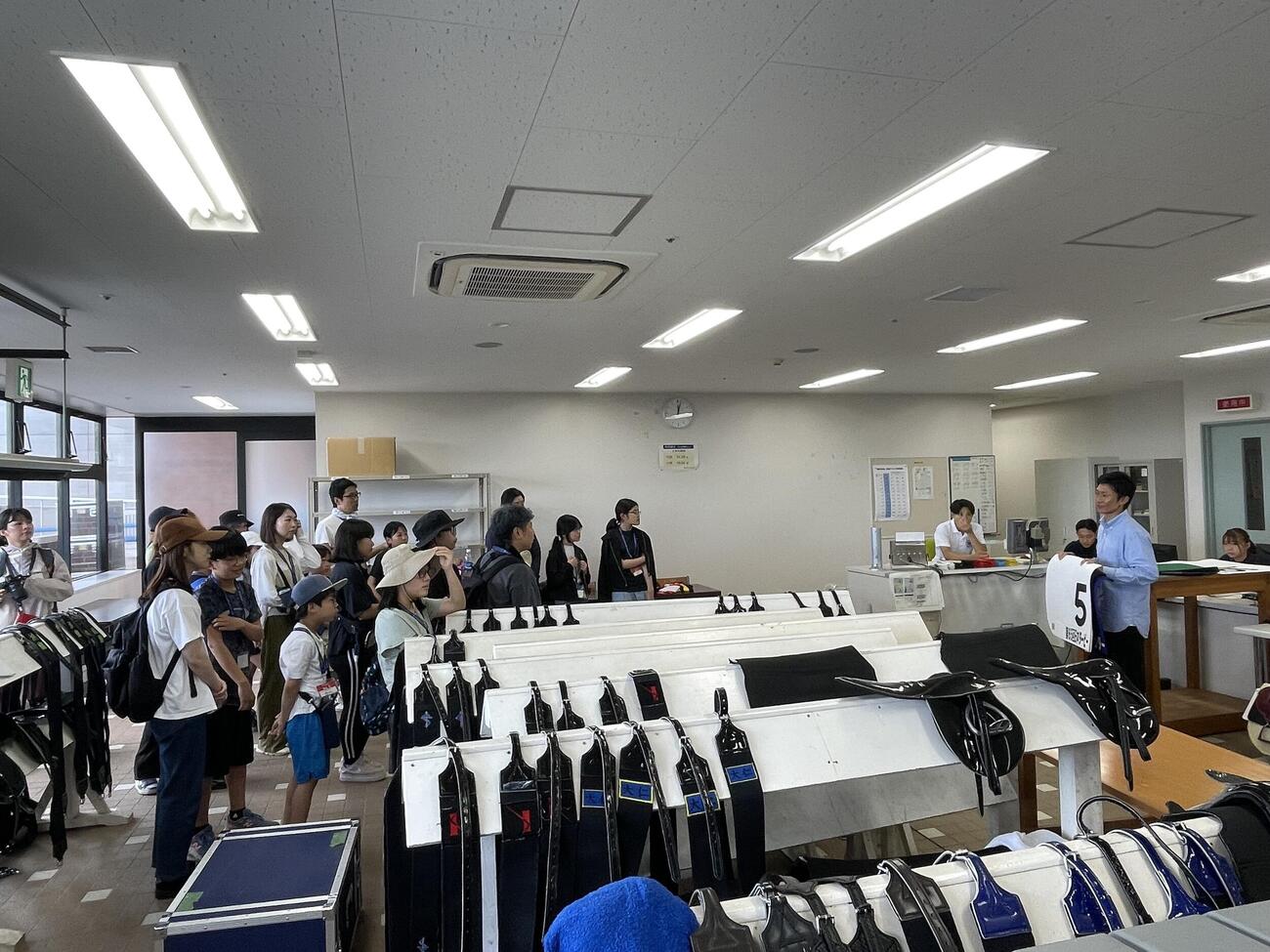 検量室内でゼッケンについて説明する荻野琢真騎手の話に参加者は興味津々
