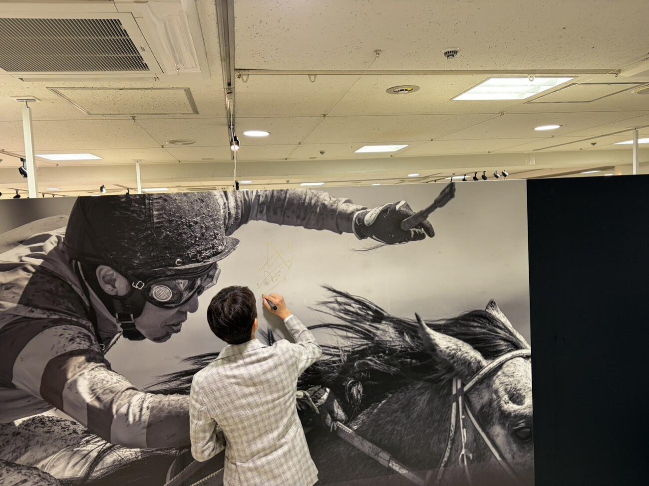 武豊展でパネルにサインする武豊騎手