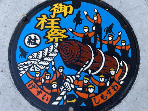 下社春宮の前の道で御柱祭の様子が描かれたマンホールのフタを見つけた
