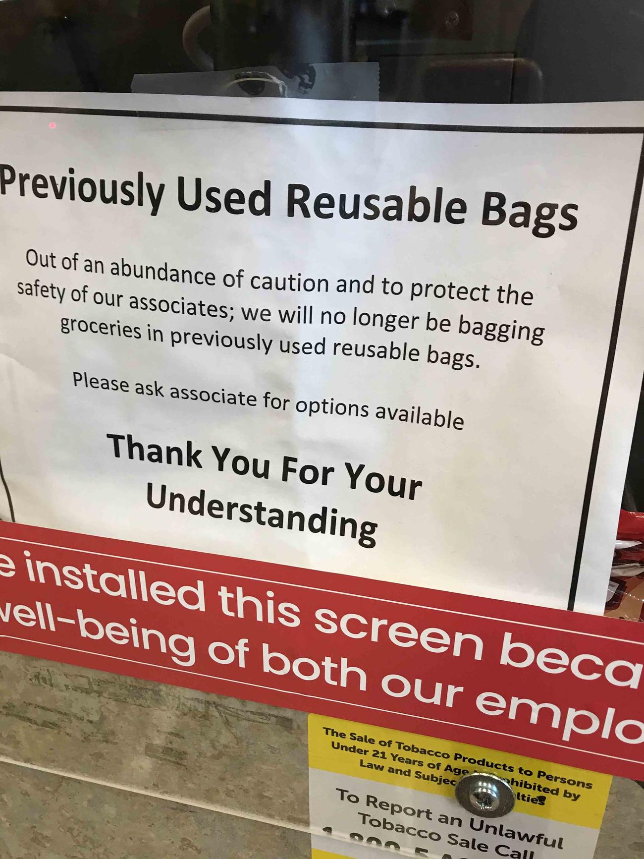 スーパーマーケットのレジに設置された感染防止対策のプラスチックの防護壁にはエコバッグ利用禁止の張り紙が