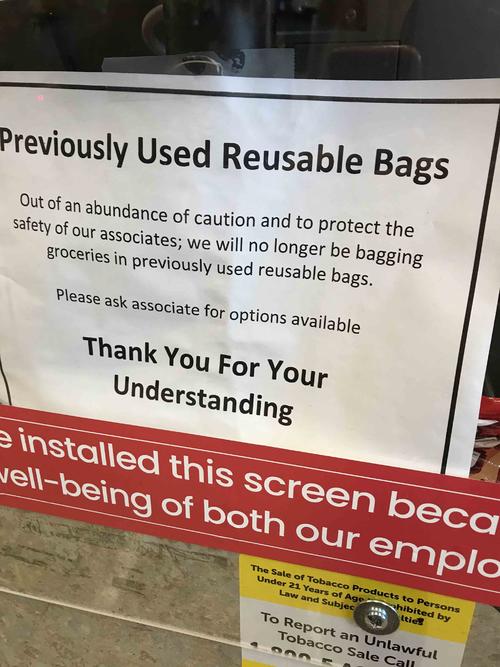 スーパーマーケットのレジに設置された感染防止対策のプラスチックの防護壁にはエコバッグ利用禁止の張り紙が