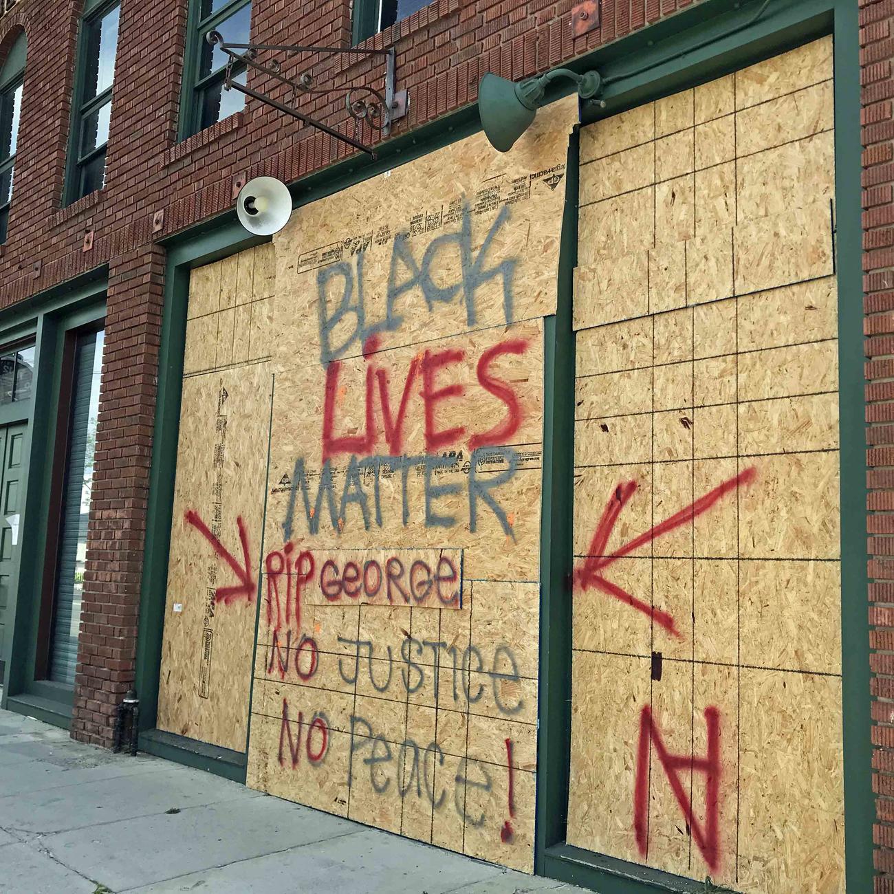防護板にBlack Lives Matterとメッセージを掲げる衣料品店。正義がない限り、平和もないと書かれています