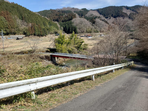 〈5〉駅から坂を下りて川を渡るといくつかの民家がある。県道は山沿いのかなたを通る