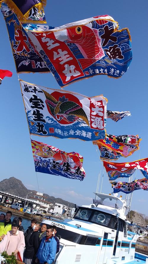 進水式の祝詞では、お祝いに贈られた大漁旗が青空の下はためいた