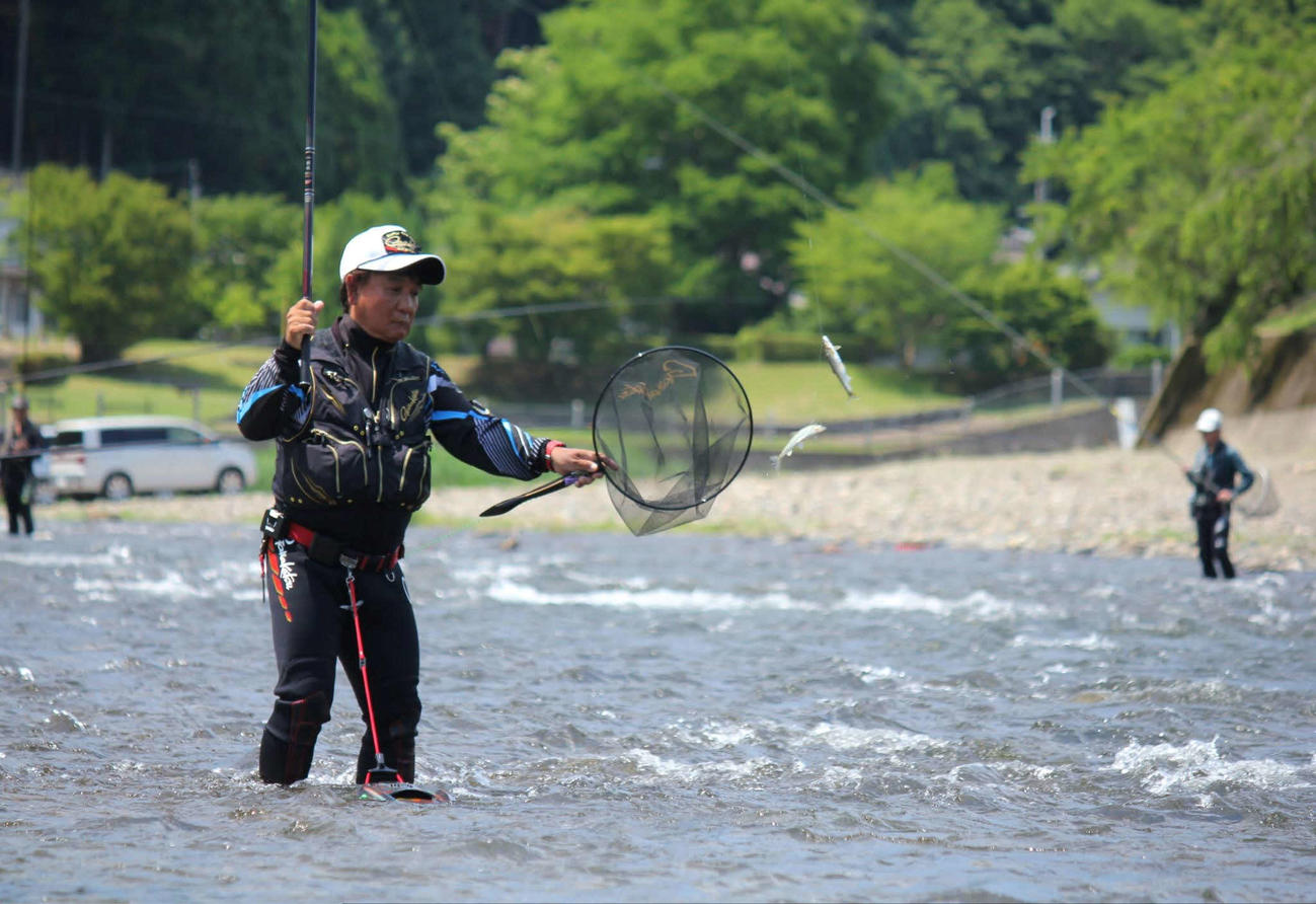 引き泳がせ釣りで野アユを掛け、タモに飛ばす筆者