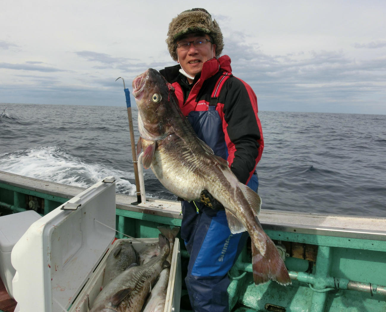 釣り上げたマダラを両手で抱え上げる坪井さん