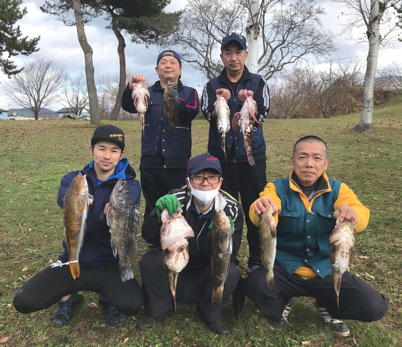 釣果のカジカなどを掲げる北海道遊釣倶楽部の、前列左から大杉和洋さん、小玉均さん、土本衛さん、後列左から藤本リポーター、佐々木由則さん