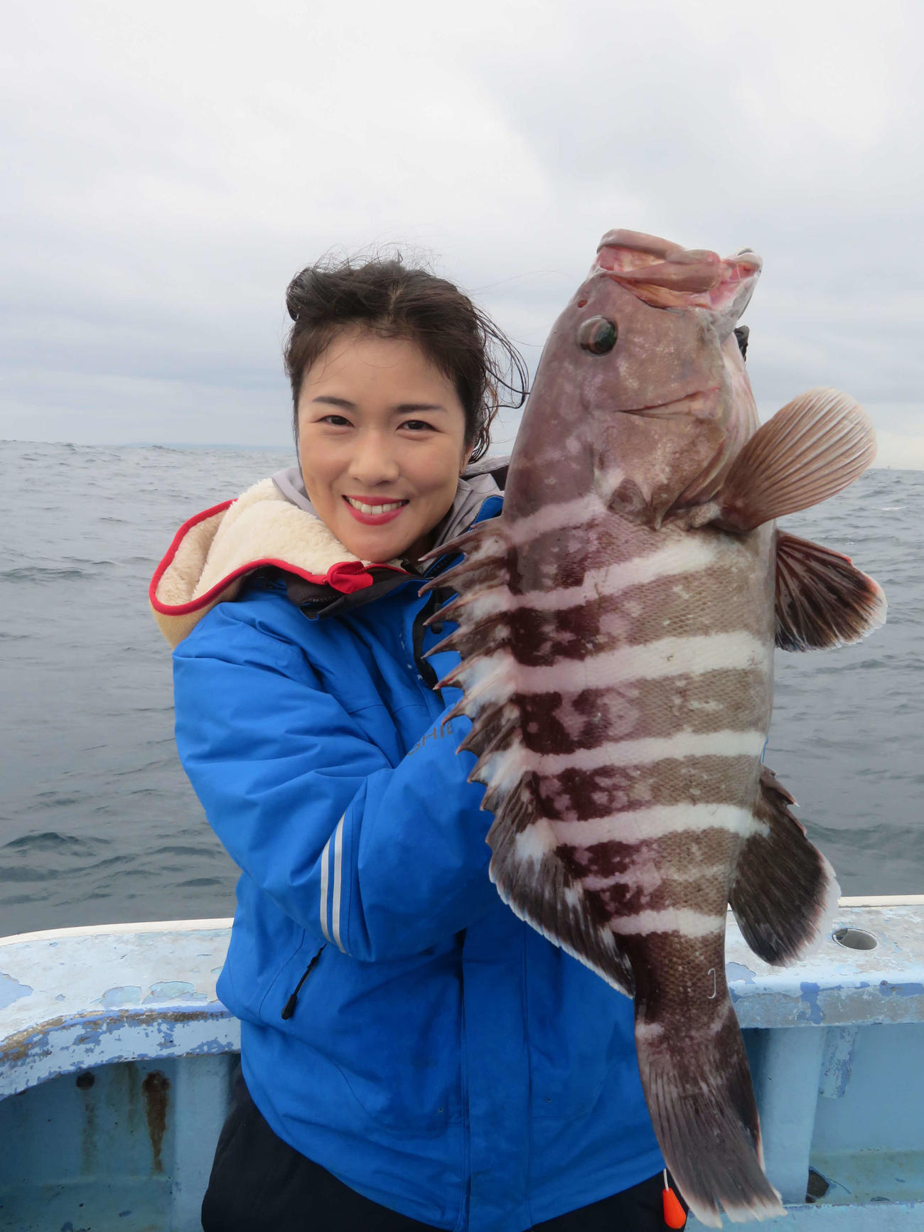人生初のアタリなしボウズ。記者が釣り上げたマハタを掲げニッコリだが、心中穏やかではかった出光仁美