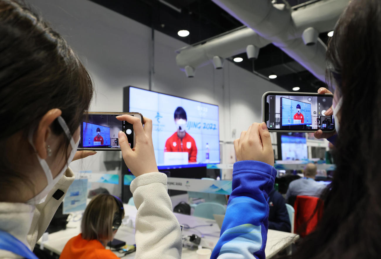 メディアセンターで羽生結弦の会見の様子を映し出すテレビ映像を撮影するボランティアスタッフ（撮影・足立雅史）
