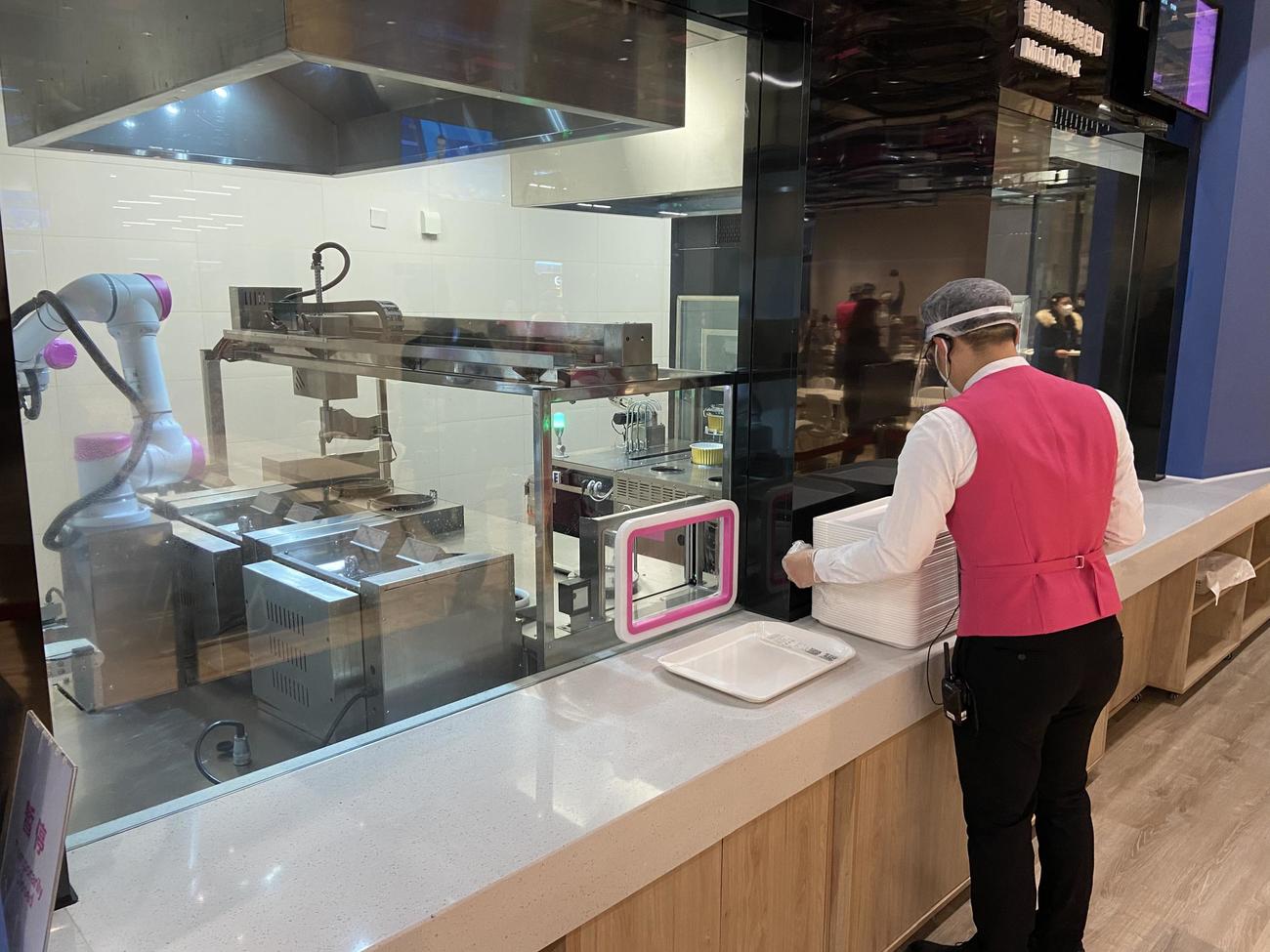 北京五輪のメインメディアセンター内にある食堂で調理するロボット。スタッフは外で待つ（撮影・松本航）