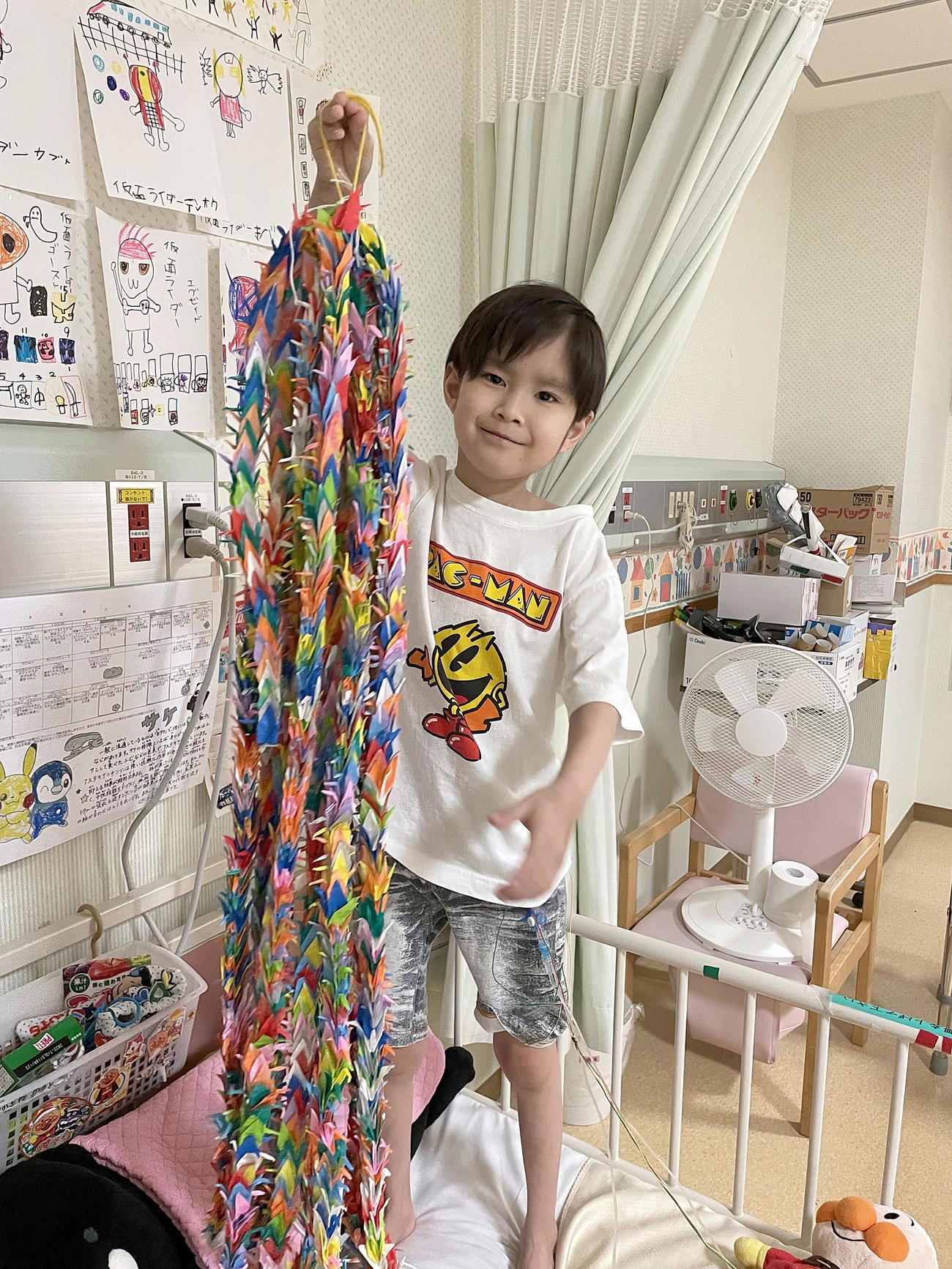 ベッドの上で千羽鶴を持って笑顔を見せる中沢維斗くん（ゆうちゃんを救う会提供）