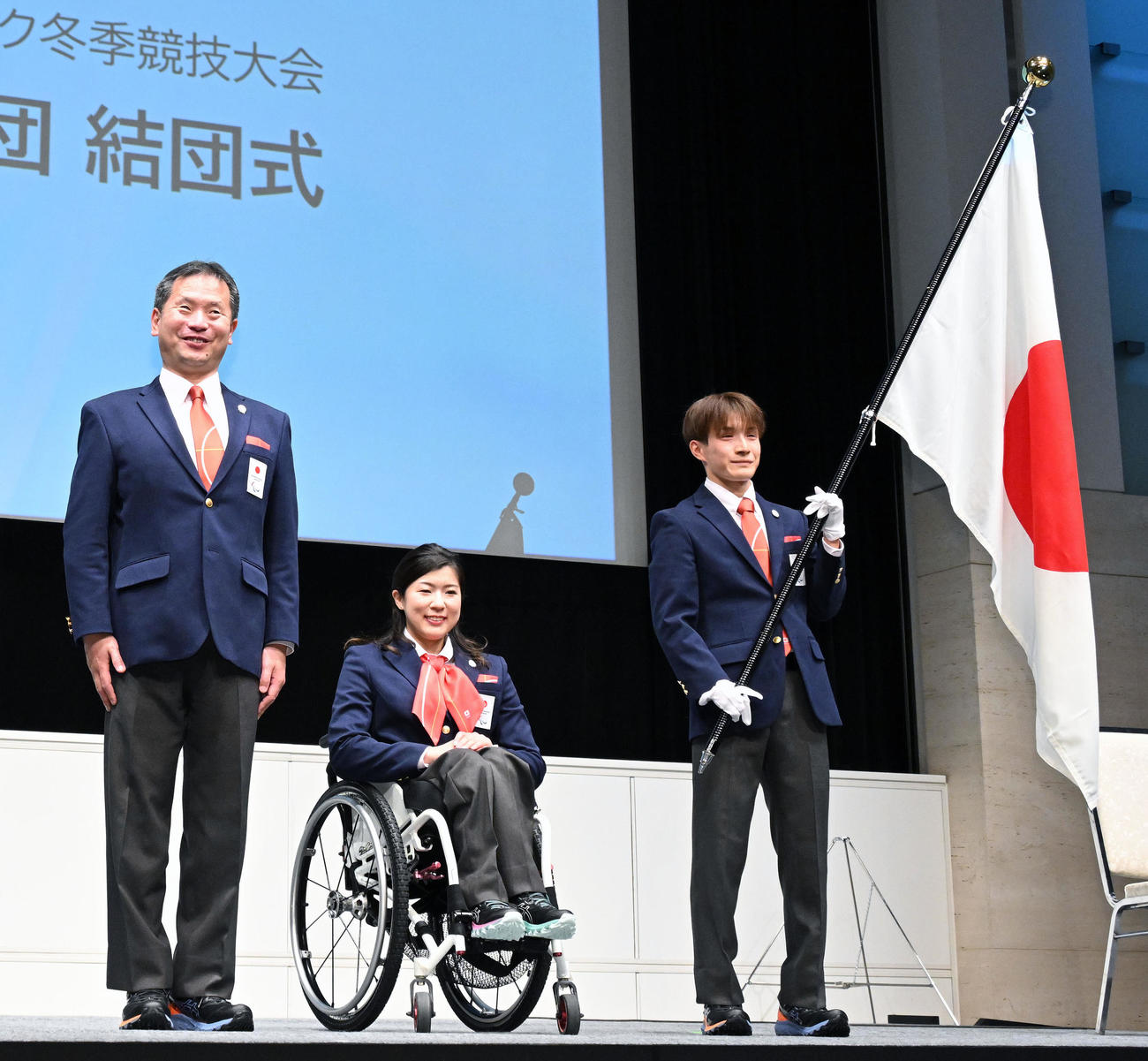結団式の団旗授与後に記念撮影する、左から河合純一団長、村岡主将、川除旗手（撮影・滝沢徹郎）