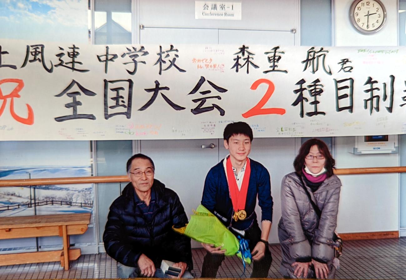 中標津空港で上風連中の仲間が作製した「全中2冠」の横断幕の前で記念撮影する左から父誠さん、森重航、母俊恵さん