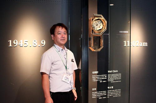 投下時刻を指す時計が展示されている長崎原爆資料館の入り口で説明をする長崎市平和推進課の大久保課長