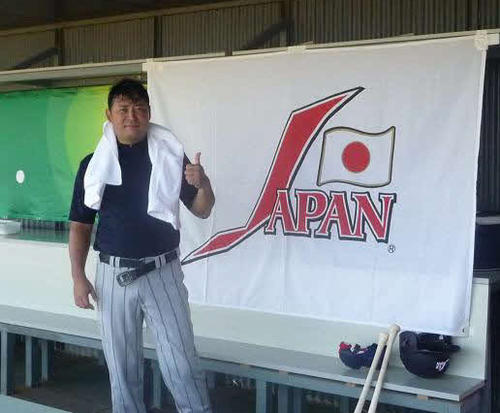 08年北京五輪野球日本代表に手伝いとして参加した光山英和氏は、日本代表のロゴの横でサムアップポーズをとる（本人提供）