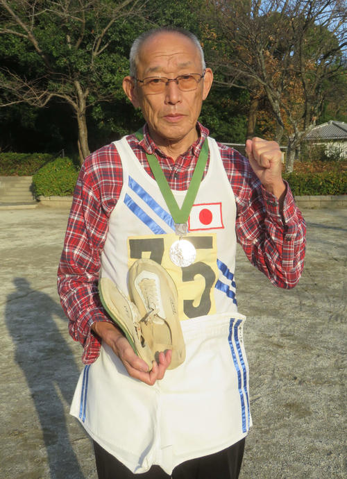君原健二さんは東京五輪時のユニホーム、シューズとメキシコ五輪の銀メダルを胸にガッツポーズ