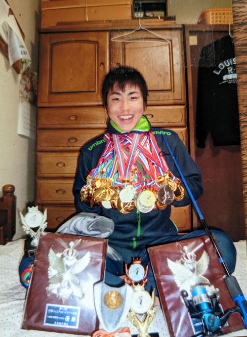 中学卒業時に小学時代から獲得したメダルを首にかけて記念撮影する新浜。大好きな釣り竿も一緒に撮影した