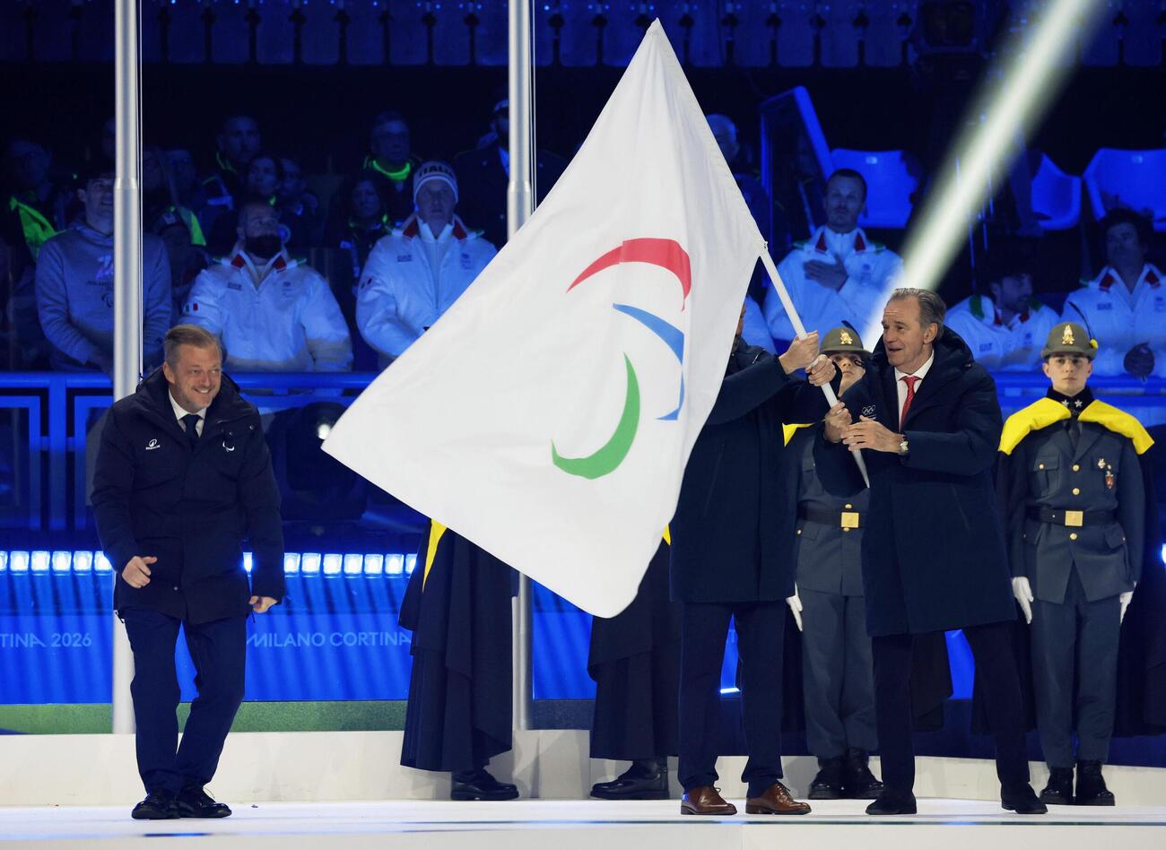 ミラノ・コルティナ冬季パラリンピックの閉会式で、次回大会の開催地フランス・アルプス地域に引き継がれたパラリンピック旗。左端はIPCのパーソンズ会長（共同）