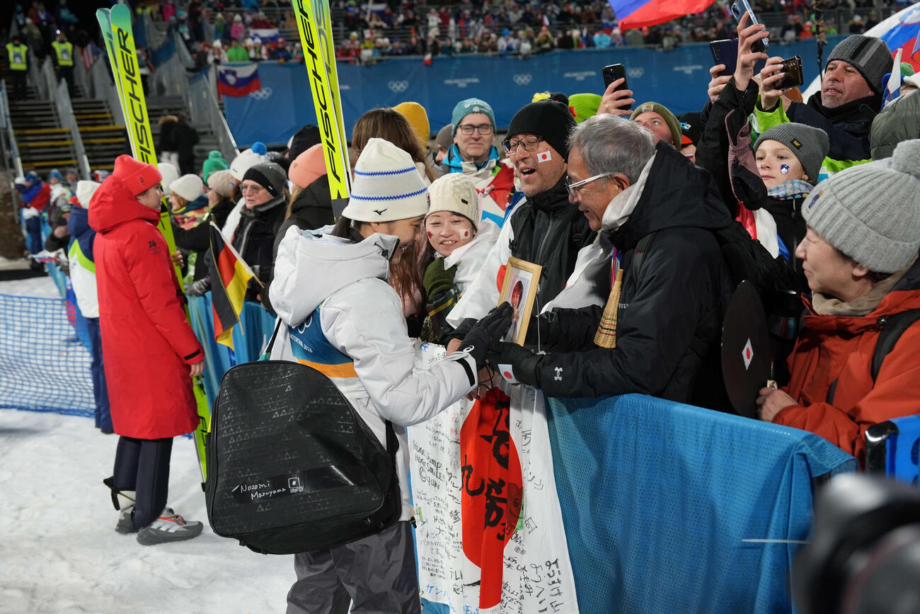 女子個人ラージヒルを終え、父守さん（右）が持つ母信子さんの写真に触れる丸山希（撮影・パオロ　ヌッチ）