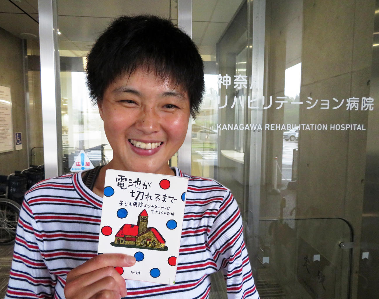 鹿沼由理恵は勤務先の神奈川リハビリテーション病院で愛読書「電池が切れるまで」を手に笑顔を見せる