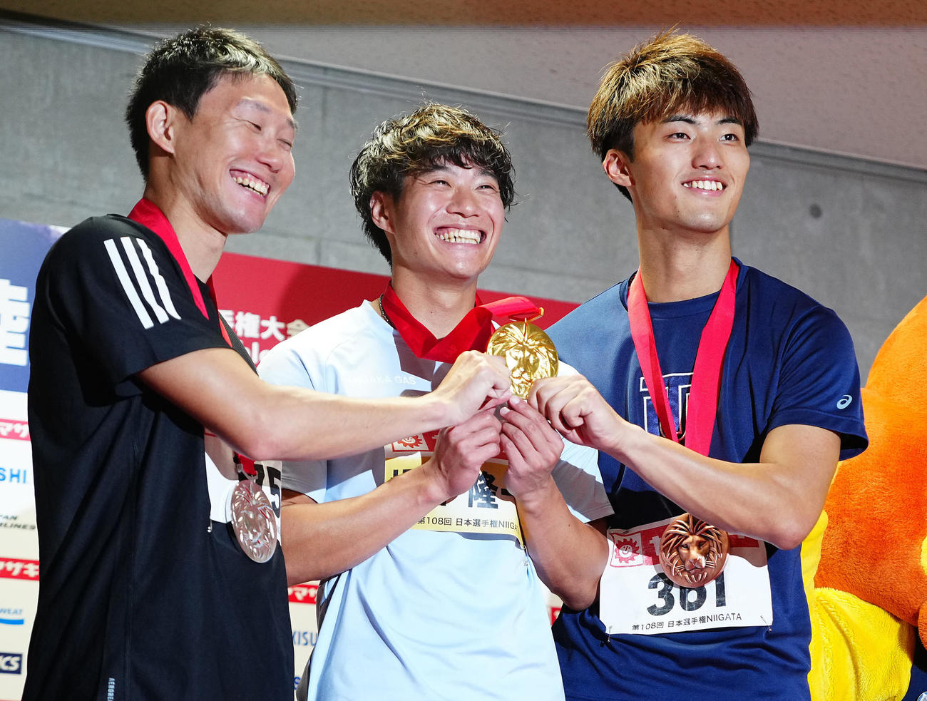 男子100メートルの表彰で1位の坂井隆一郎（中央）は柳田大輝（右）、東田旺洋に金メダルをつかまれ笑顔を見せる（2024年6月30日）